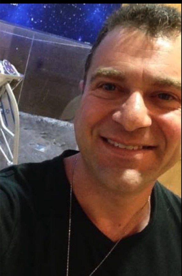 Naf smiling in a black T-shirt in front of a starry space mural