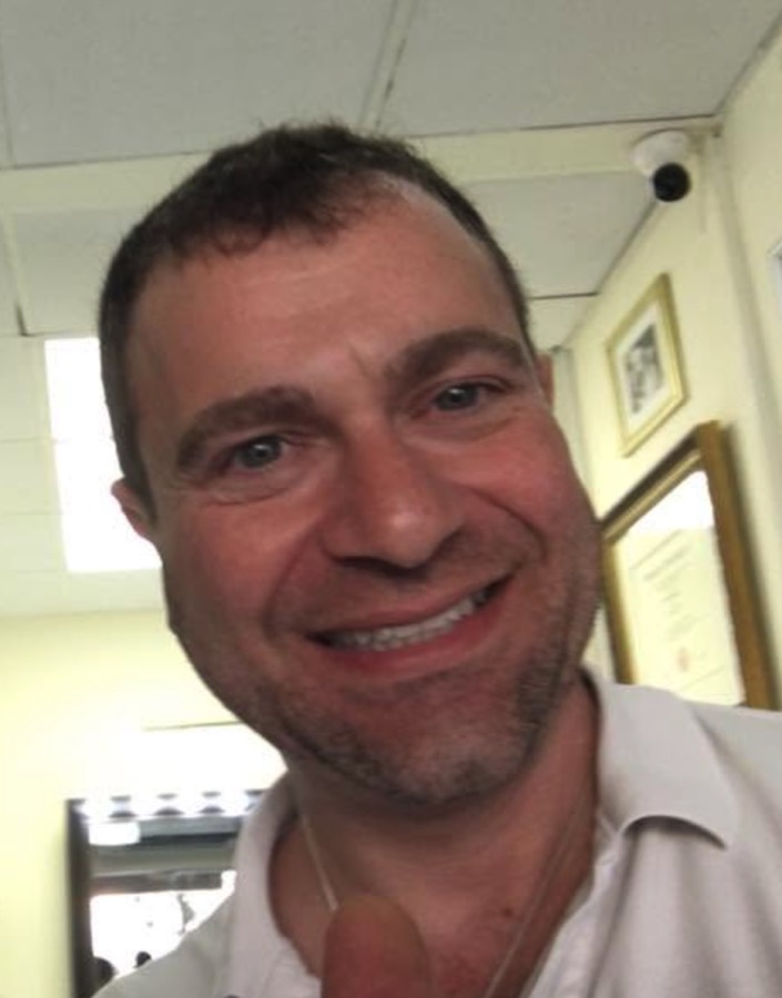 Naf grinning into the camera in a bright office with framed certificates on the wall